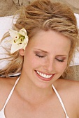 Close-up of pretty woman with flower in her hair, smiling with eyes closed, overhead view