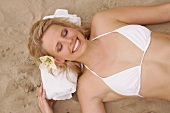 Overhead view of pretty woman in white bikini lying on sand, smiling with eyes closed