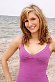 Portrait of beautiful woman wearing purple top standing on beach, smiling