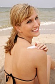 Close-up of attractive blonde woman sitting on beach and applying cream on back