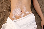 Close-up of woman lying on sand with salt crystals on belly