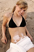 Portrait of pretty woman wearing lingerie lying on sand with salt crystals on belly