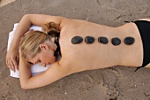 Rear view of blonde woman lying on beach with stones on her back