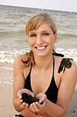 Portrait of attractive woman in black bikini standing on beach with algae in hands