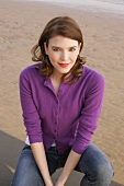 Portrait of beautiful woman wearing purple sweater and jeans sitting on beach, smiling