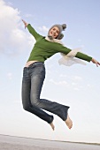 Beautiful woman wearing green sweater, jeans and cap jumping in air, smiling widely