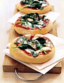 Close-up of mini-pizzas with spinach on white napkins, wooden board