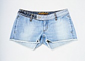 Close-up of pair of blue denim hot pants on white background