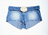 Close-up of pair of blue denim hot pants with oval buckle on white background