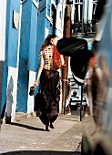 Woman wearing polka dots top walking on street while carrying mesh bag on shoulder