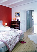 Bedroom with red and white walls, pink bedspread, floorboards and open door