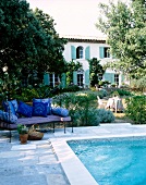 Sofa am Pool, im Hintergrund Haus umgeben von Bäumen.