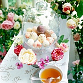 Pralinen unter einer Glashaube auf einem Tisch im Garten, Blumen. x