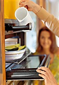 Frau gießt Wasser in Dampfgarer aus Karaffe in Weiß, Küchengerät
