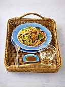 Chicken noodles with sauce and glass of water on plate in wicker basket