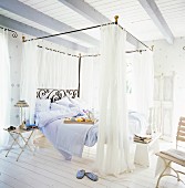 A romantic, country-style bedroom in white with a metal four poster bed
