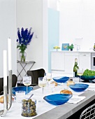 Gedeckter Tisch im Zimmer in Weiß, Farbakzente in Blau, unscharf