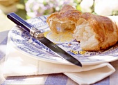 Halbiertes Croissant auf einem Teller, daneben ein Messer.