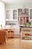 Einblick in die Küche, weiße Einbauküche, Holztisch und Korbstühle.