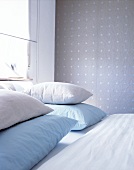 Close-up of blue and cream pillows on double bed against textile wallpaper
