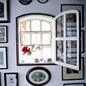 Kleines Fenster in einer weißen mit Bildern behangenen Wand.