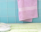 White slippers on bathroom mat against blue tiled wall with pink towel