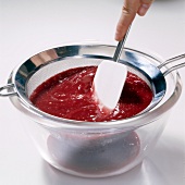 Hand straining fruit puree with sieve in glass bowl