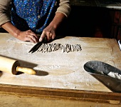 Woman slicing rolled buckwheat dough with knife on table, step 5