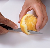 Close-up orange being peeled with knife