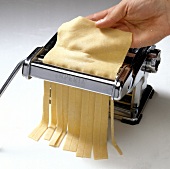 Pappardelle pasta dough being cut into stripes in pasta machine