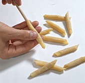 Hand pulling wrapped dough from round timber for preparing garganelli pasta, step 3