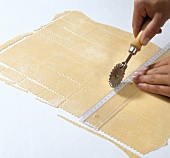 Hand cutting dough with pastry cutter and ruler for preparing farfalle pasta, step 1