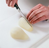 Hand cutting halved peeled pear with knife on cutting board