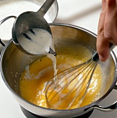 Vanilla milk being poured in egg and sugar mixture in casserole