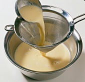 Cream being poured through sieve in bowl