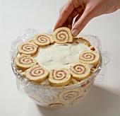 Roulade biscuit slices being arranged on cream in bowl
