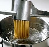 Teigwaren. Teigfäden werden in kochendes Wasser gedrückt