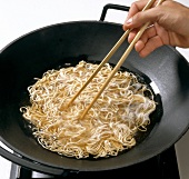 Noodles being separated with chopstick in wok, step 2