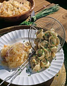 Close-up of pelmeni with mushrooms and coleslaw on plate with skimmer