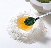 Mashed basil being added to flour and egg yolks