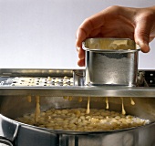 Close-up of pasta dough being dripped through sparrow slicer into water