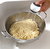 Boiled noodles being washed with water in pot while preparing bami goreng pasta, step 2