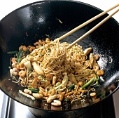 Boiled noodles and various ingredients in wok while preparing bami goreng pasta, step 6
