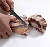 Oxtail being cut with knife while preparing braised oxtail, step 1