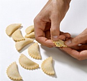Hands pressing edge of stuffed pasta dough while preparing tortelloni, step 3