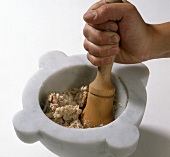 Hand crushing walnut with pestle in mortar for preparation of walnut sauce, step 1