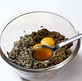 Close-up of oil being added to minced meat and egg yolks in bowl