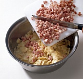 Chopped ham being added to bowl of pasta while preparing schinkenfleckerln, step 1
