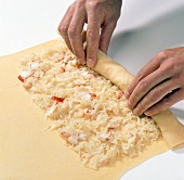 Hands rolling noodle dough with filling
