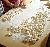 Woman's hands cutting rolled dough into pieces for preparation of gnocchi, step 3